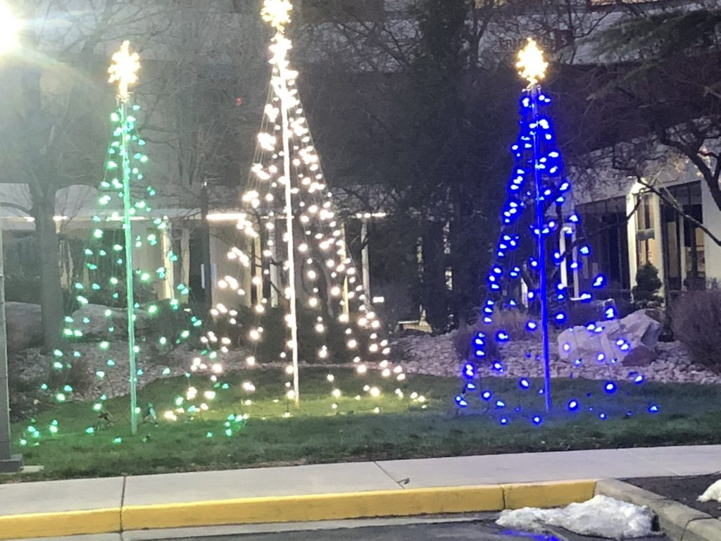 Three light trees in green, white and blue outside a building
