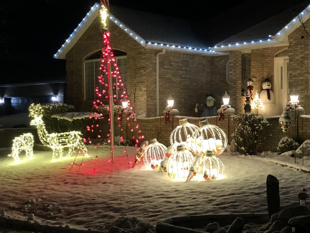 Brick home at night with a lit red tree, glowing reindeer, light-up ornaments and roofline lights in the snow