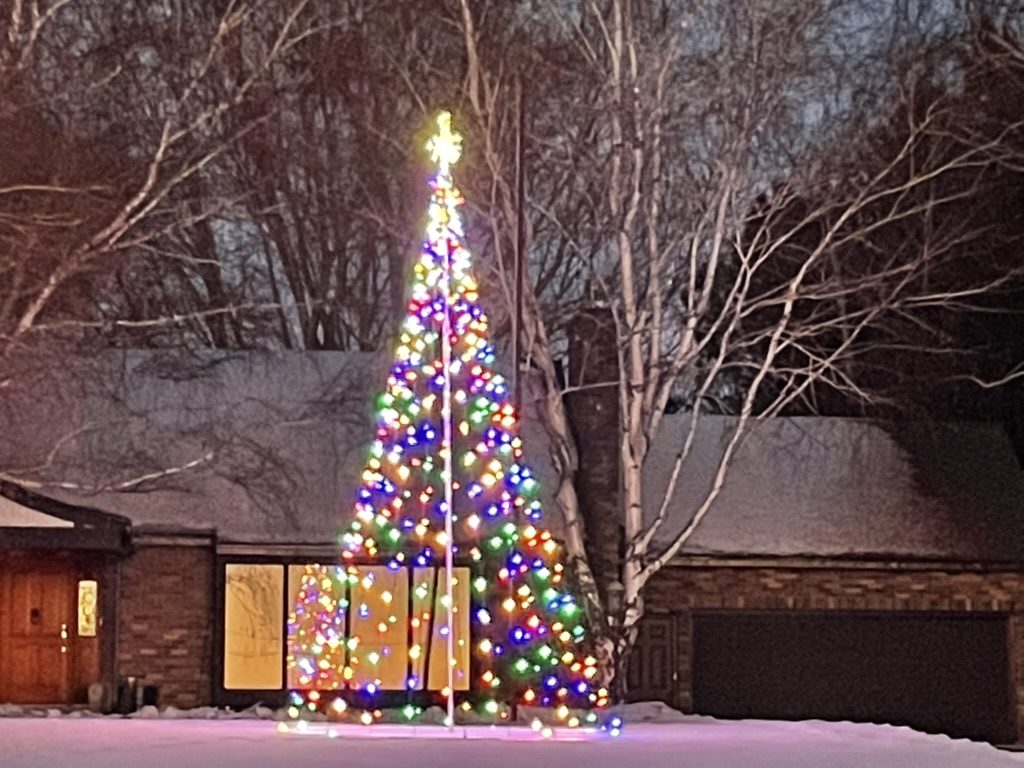 Tall multicolor light tree in a snowy front yard at night